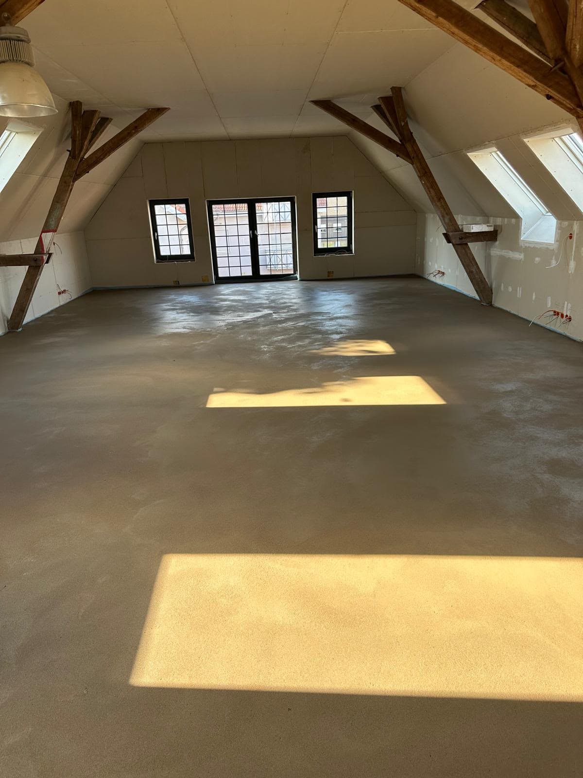 Frisch verlegter Estrich im ausgebauten Dachgeschoss mit Balkontür